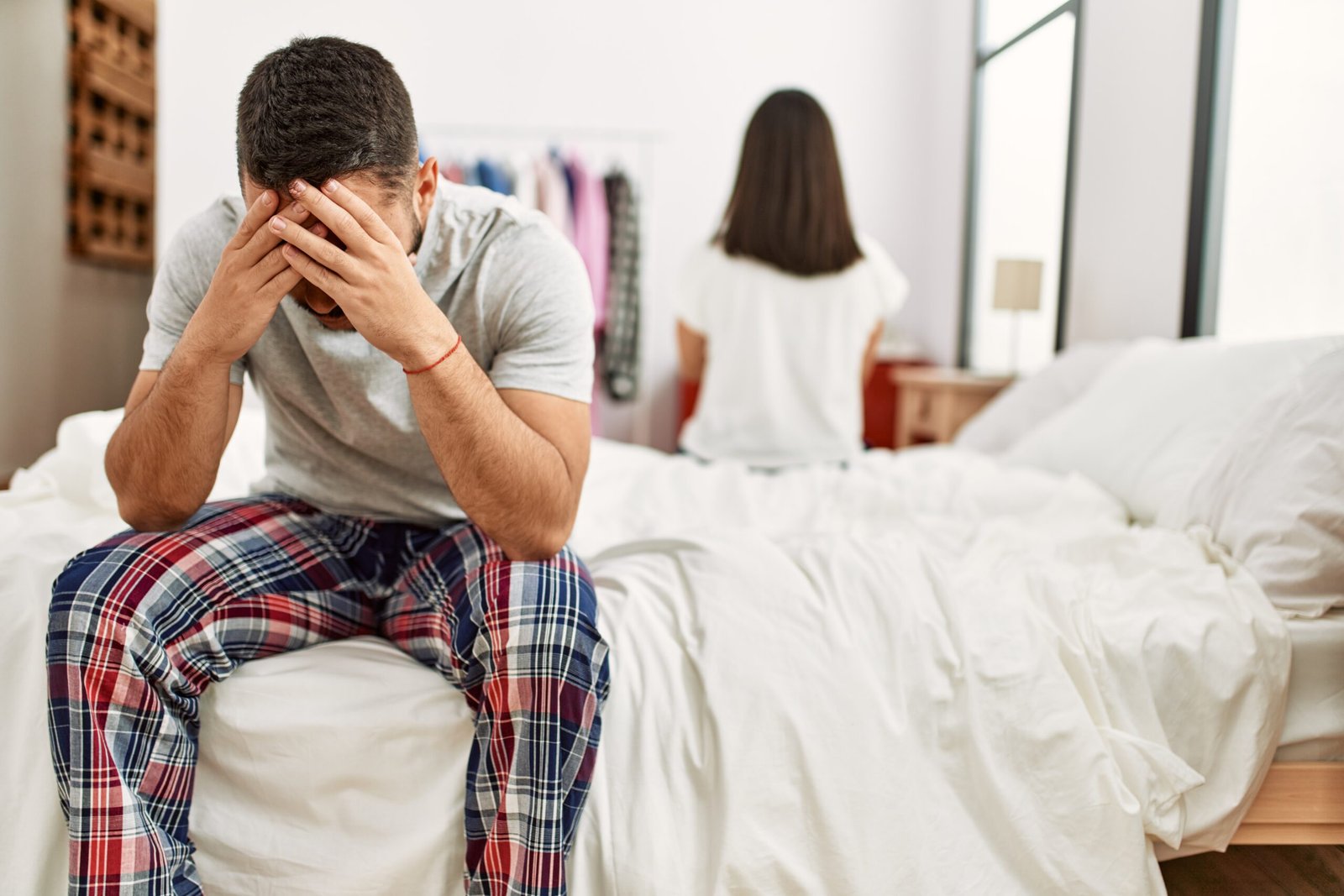 Young latin couple in trouble. Sitting on the bed with hands on head.